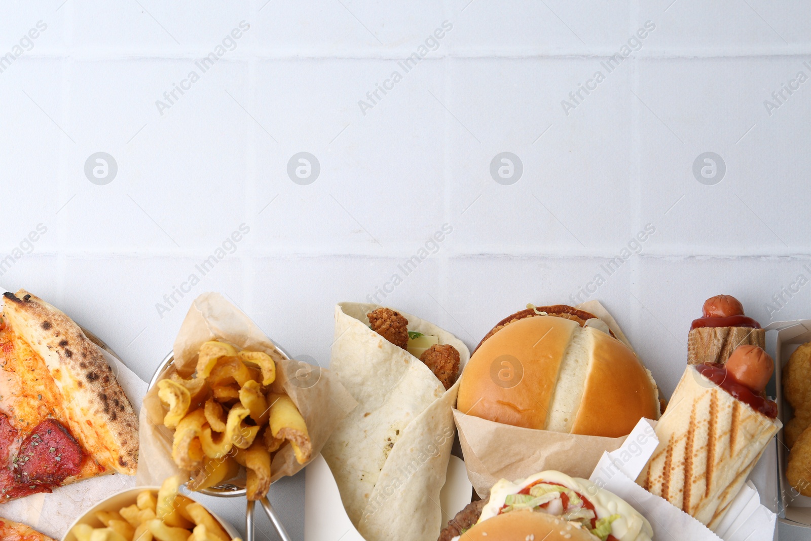 Different delicious fast food on white tiled table, flat lay. Space for text Photo of Different delicious fast food on white tiled table, flat lay. Space for text