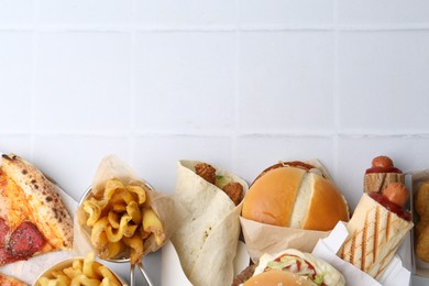 Photo of Different delicious fast food on white tiled table, flat lay. Space for text