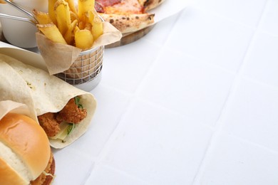 Photo of Different delicious fast food on white tiled table, closeup. Space for text