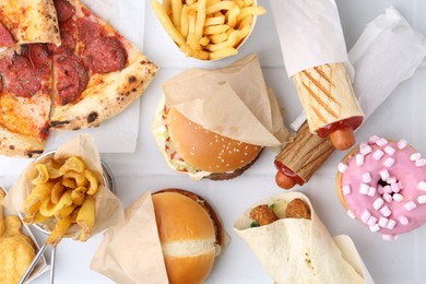 Photo of Different delicious fast food on white tiled table, flat lay