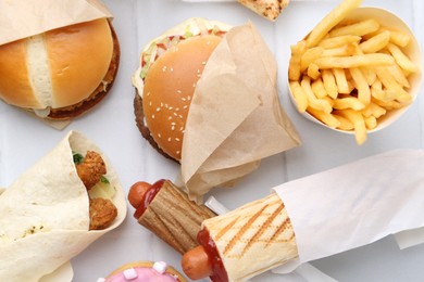 Photo of Different delicious fast food on white tiled table, flat lay