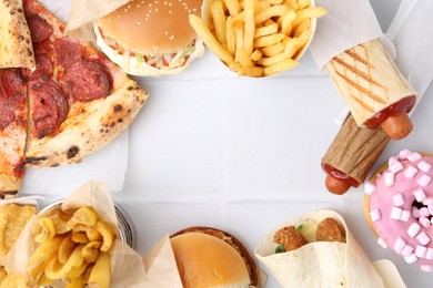 Photo of Different delicious fast food on white tiled table, flat lay. Space for text