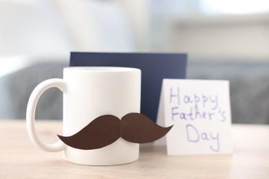 Photo of Happy Father's Day card, cup with mustache and envelope on wooden table at home, closeup