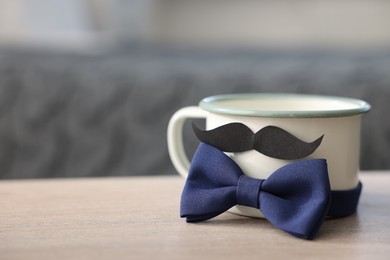 Photo of Happy Father's Day. Cup with mustache and bowtie on wooden table at home, closeup. Space for text