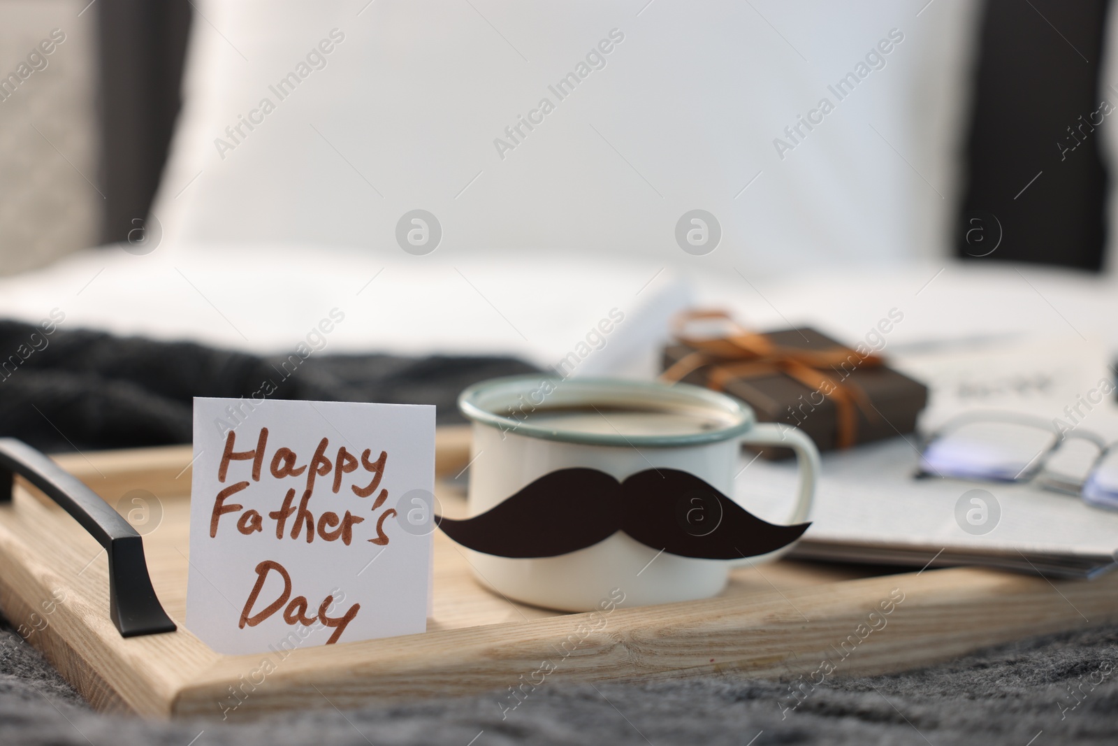 Happy Father's Day card and cup with mustache on bed at home, closeup. Space for text Photo of Happy Father's Day card and cup with mustache on bed at home, closeup. Space for text