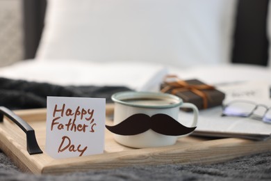 Photo of Happy Father's Day card and cup with mustache on bed at home, closeup. Space for text