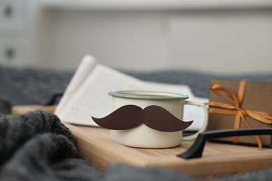 Photo of Happy Father's Day. Cup with mustache and gift on bed at home, closeup