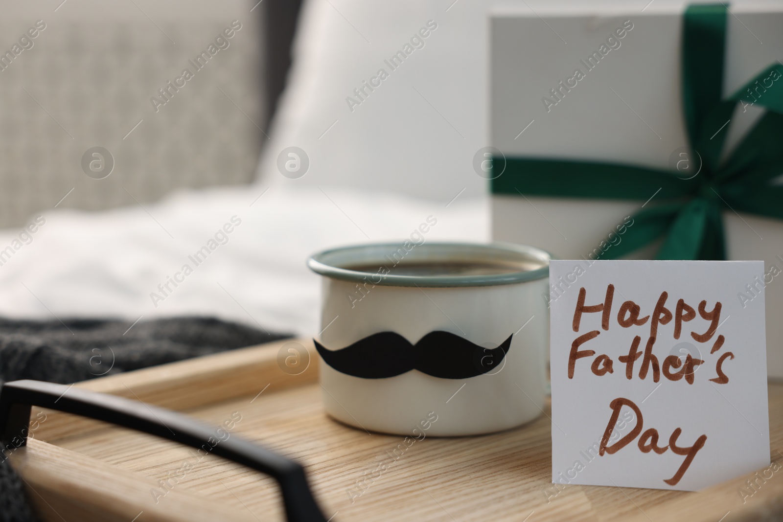 Happy Father's Day card, cup with mustache and gift on bed at home, closeup. Space for text Photo of Happy Father's Day card, cup with mustache and gift on bed at home, closeup. Space for text