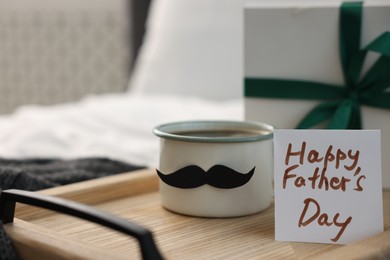 Photo of Happy Father's Day card, cup with mustache and gift on bed at home, closeup. Space for text