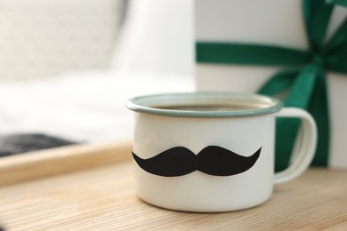 Photo of Happy Father's Day. Cup with mustache and gift on bed at home, closeup. Space for text