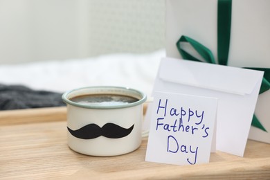 Photo of Happy Father's Day card, cup with mustache, gift and envelope on bed at home, closeup