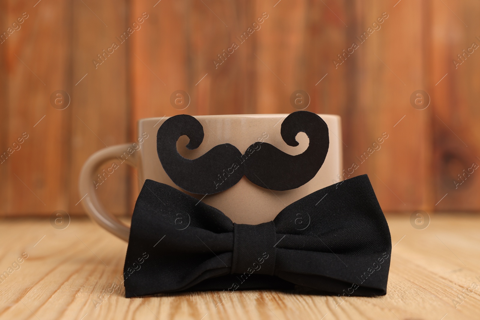 Happy Father's Day. Cup with mustache and bowtie on wooden table, closeup Photo of Happy Father's Day. Cup with mustache and bowtie on wooden table, closeup