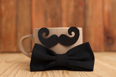 Photo of Happy Father's Day. Cup with mustache and bowtie on wooden table, closeup
