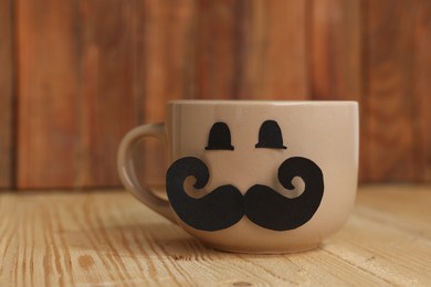 Photo of Happy Father's Day. Cup with paper face on wooden table, closeup