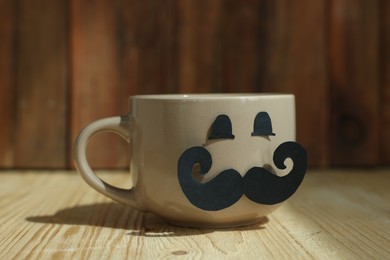 Photo of Happy Father's Day. Cup with paper face on wooden table, closeup