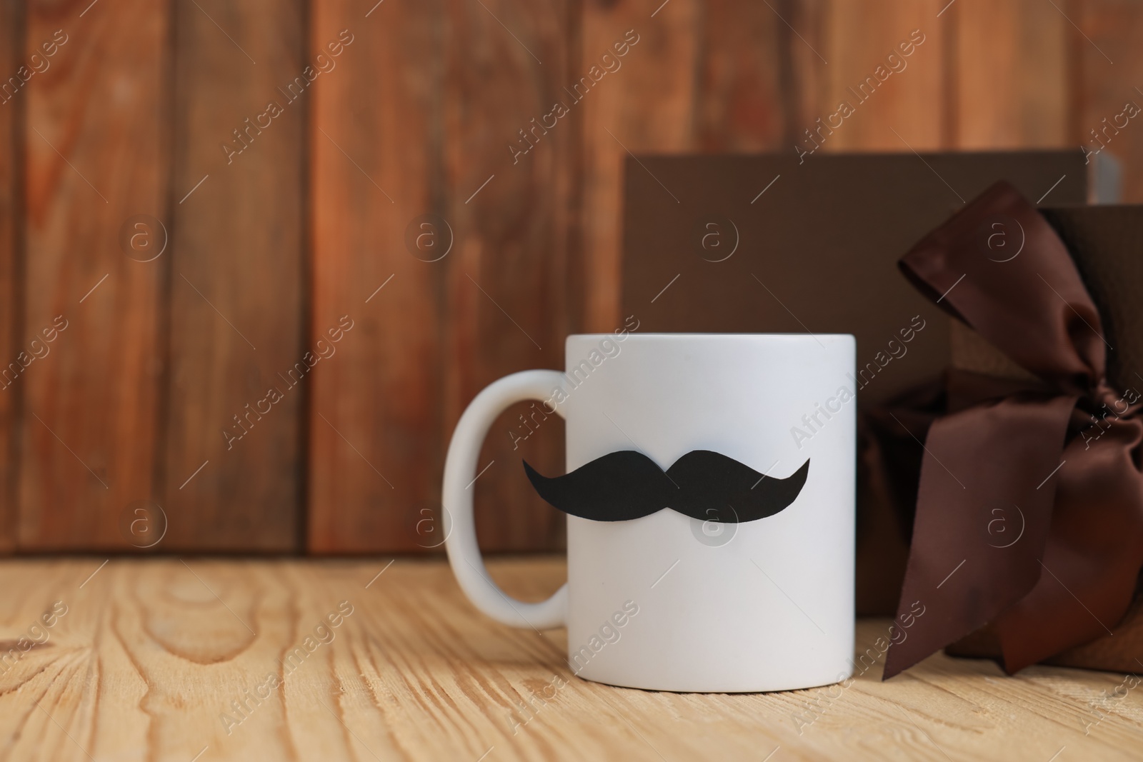 Happy Father's Day. Cup with mustache and gift on wooden table, closeup. Space for text Photo of Happy Father's Day. Cup with mustache and gift on wooden table, closeup. Space for text