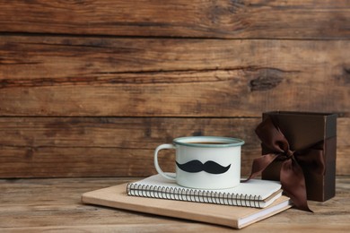 Photo of Happy Father's Day. Cup with mustache, notebooks and gift on wooden table. Space for text