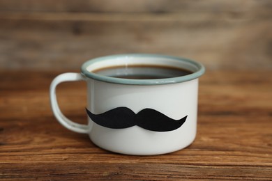 Photo of Happy Father's Day. Cup with mustache on wooden table, closeup