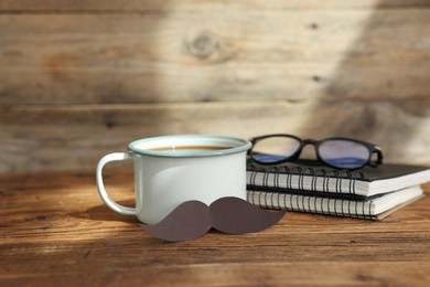 Photo of Happy Father's Day. Cup with mustache, notebooks and glasses on wooden table. Space for text