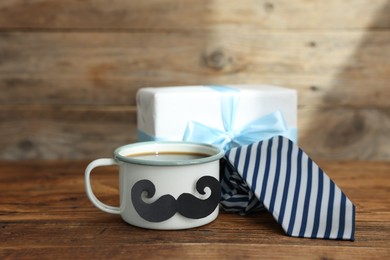 Photo of Happy Father's Day. Cup with mustache, tie and gift on wooden table