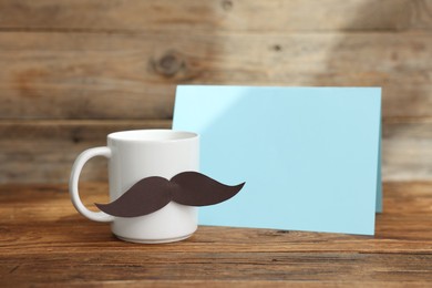 Photo of Happy Father's Day. Cup with mustache and card on wooden table. Space for text