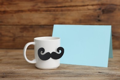 Photo of Happy Father's Day. Cup with mustache and card on wooden table. Space for text