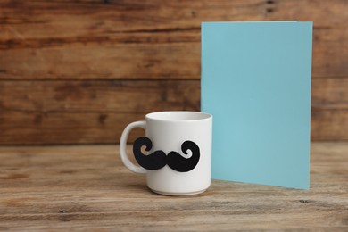 Photo of Happy Father's Day. Cup with mustache and card on wooden table. Space for text