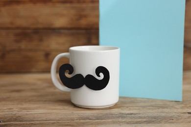 Photo of Happy Father's Day. Cup with mustache and card on wooden table. Space for text