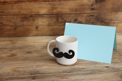 Photo of Happy Father's Day. Cup with mustache and card on wooden table. Space for text
