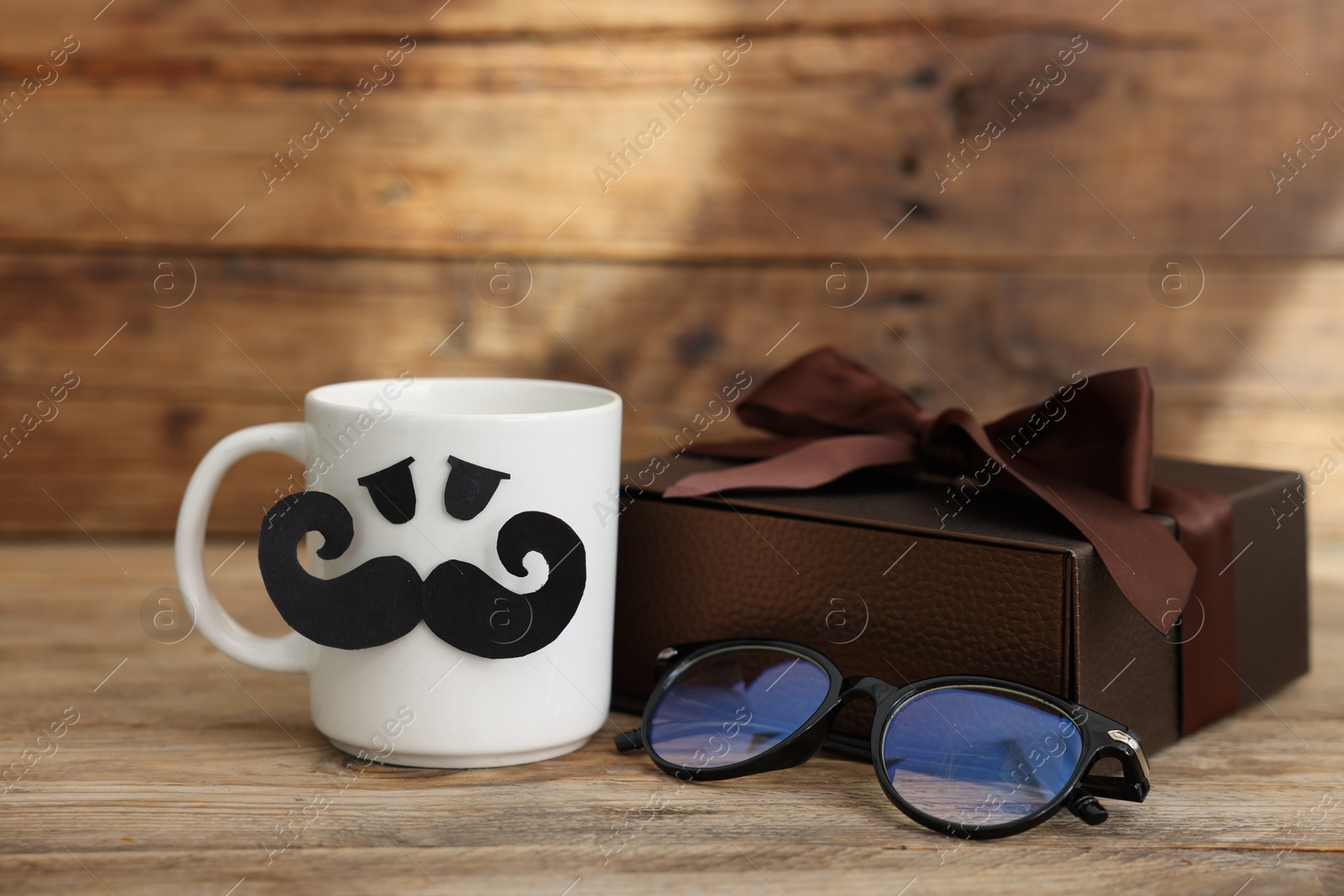 Happy Father's Day. Cup with paper face, gift and glasses on wooden table Photo of Happy Father's Day. Cup with paper face, gift and glasses on wooden table