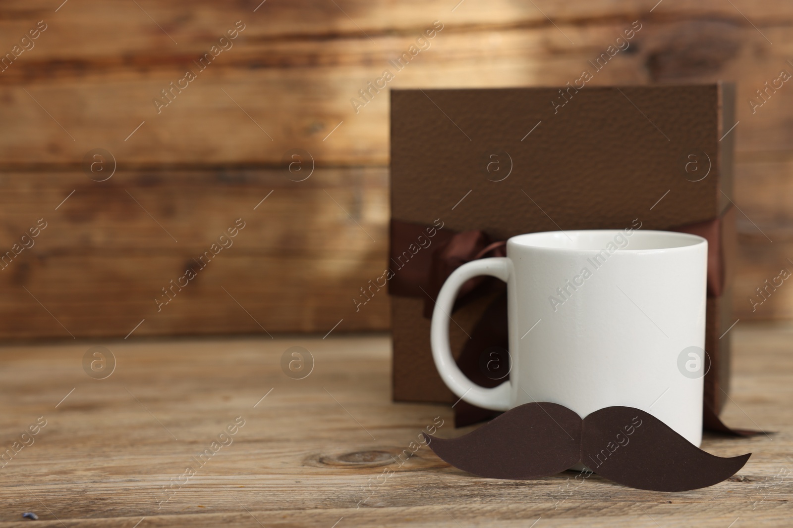 Happy Father's Day. Cup with mustache and gift on wooden table. Space for text Photo of Happy Father's Day. Cup with mustache and gift on wooden table. Space for text