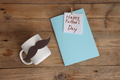 Photo of Happy Father's Day card and cup with mustache on wooden table, flat lay