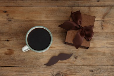 Photo of Happy Father's Day. Cup with mustache and gift on wooden table, flat lay