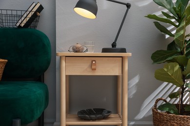 Photo of Wooden side table with glass of water, lamp and glasses indoors
