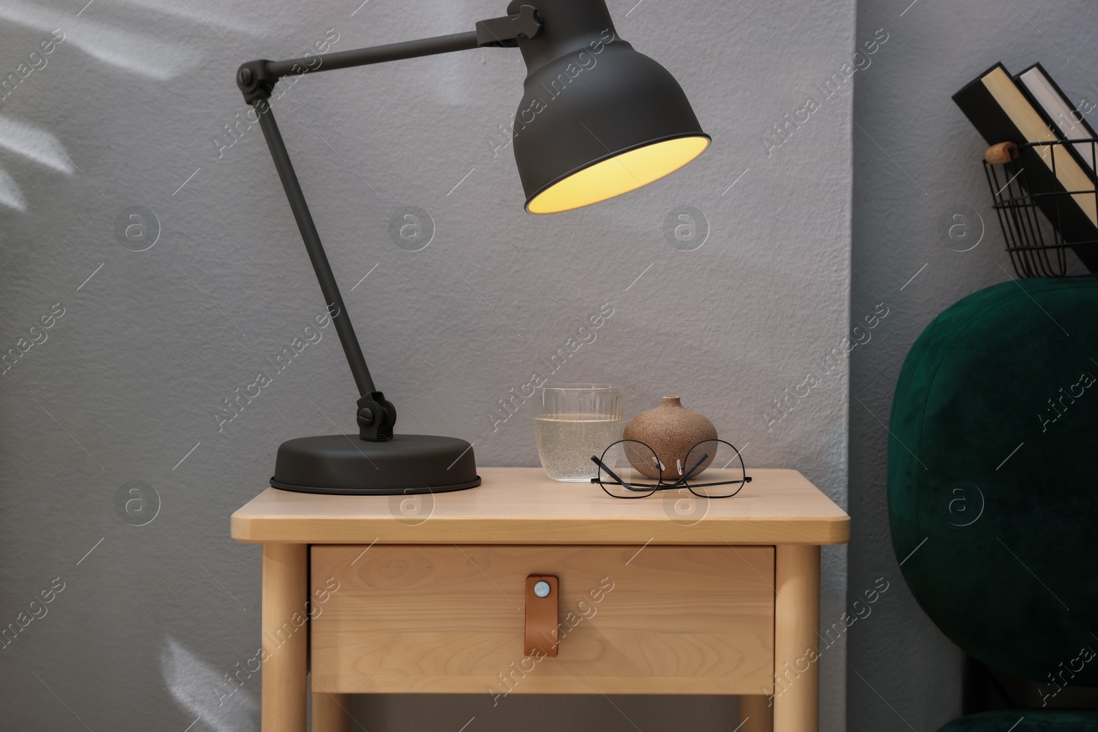 Photo of Wooden side table with glass of water, lamp and glasses indoors, closeup