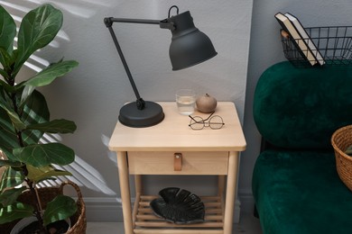 Photo of Wooden side table with glass of water, lamp and glasses indoors