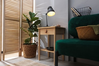 Photo of Wooden side table with glass of water, lamp and glasses indoors, low angle view