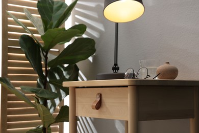 Photo of Wooden side table with glass of water, lamp and glasses indoors, closeup