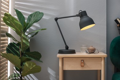 Photo of Wooden side table with glass of water, lamp and glasses indoors