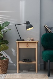 Photo of Wooden side table with glass of water, lamp and glasses indoors
