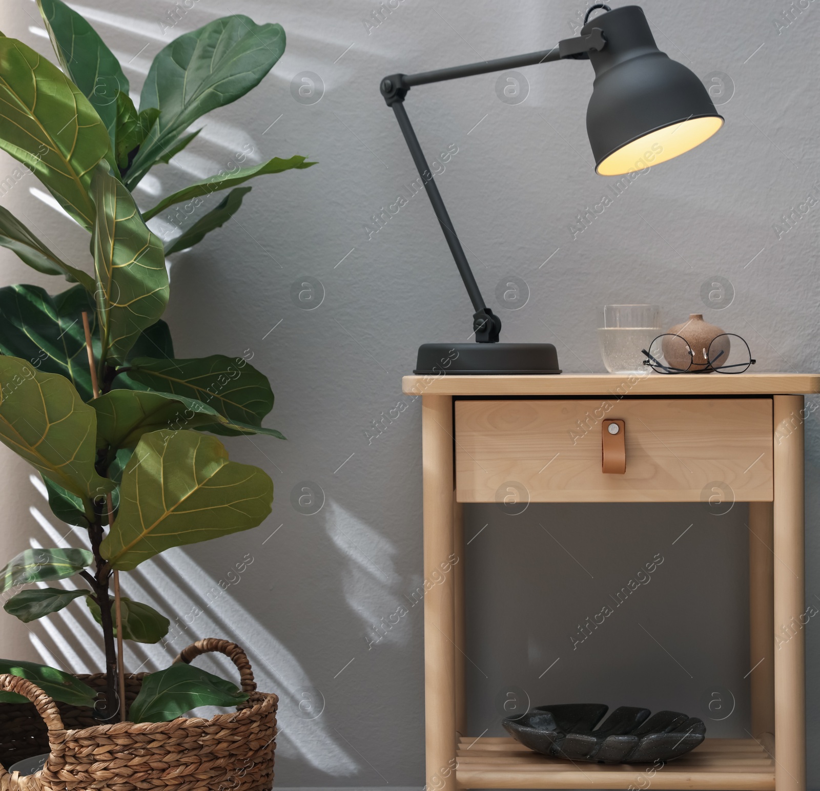 Photo of Wooden side table with glass of water, lamp and glasses indoors
