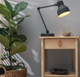 Photo of Wooden side table with glass of water, lamp and glasses indoors