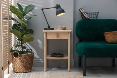 Photo of Wooden side table with glass of water, lamp and glasses indoors