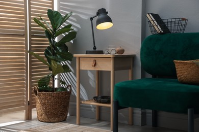 Photo of Wooden side table with glass of water, lamp and glasses indoors