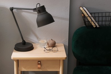 Photo of Wooden side table with glass of water, lamp and glasses indoors