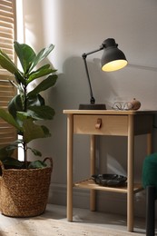Photo of Wooden side table with glass of water, lamp and glasses indoors
