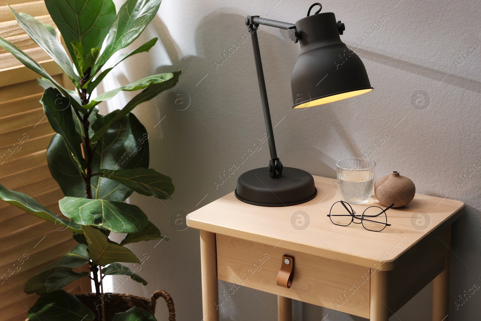 Photo of Wooden side table with glass of water, lamp and glasses indoors, closeup