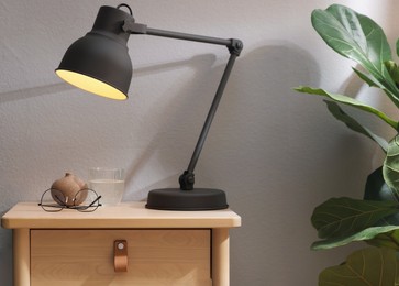 Photo of Wooden side table with glass of water, lamp and glasses indoors, closeup