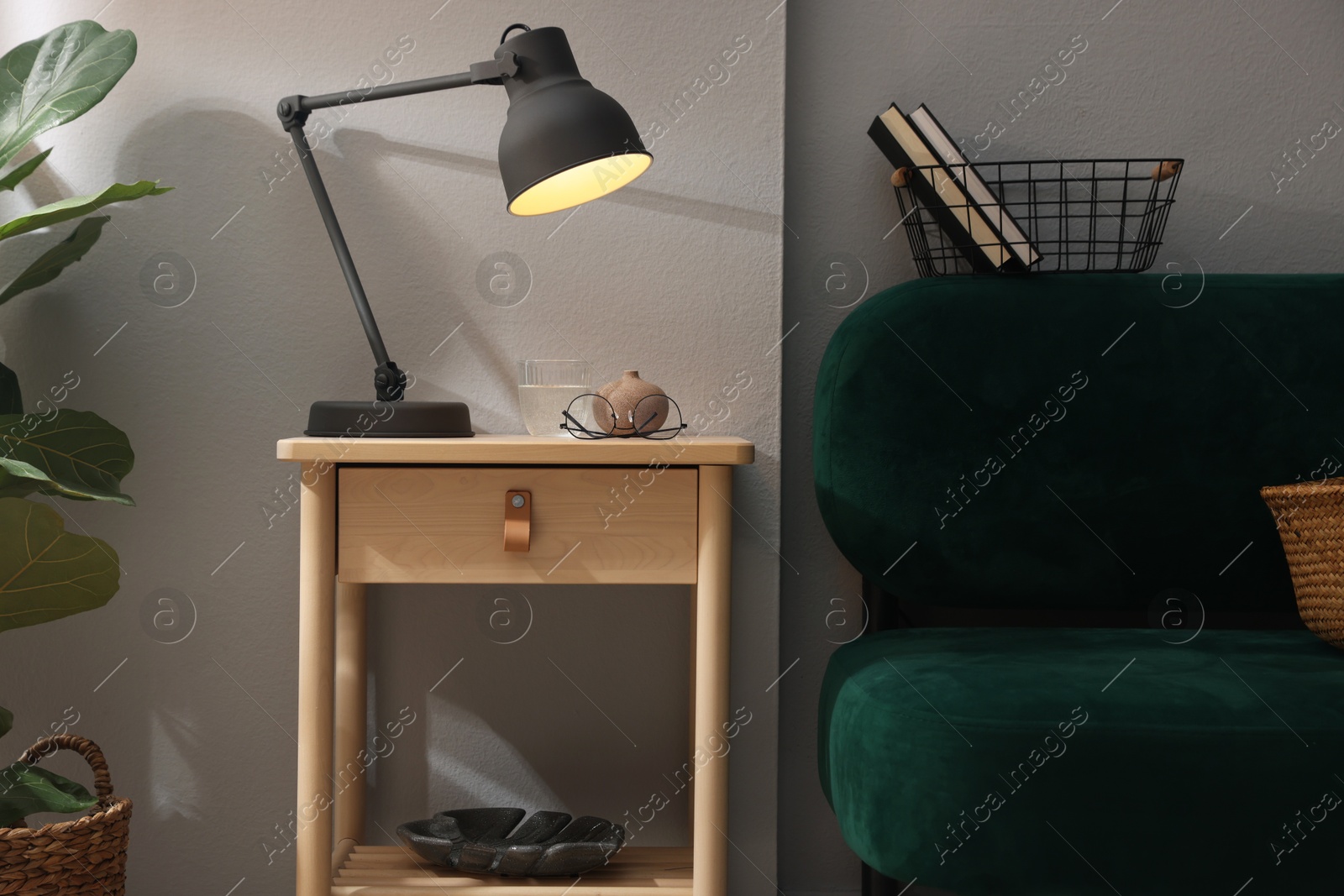 Wooden side table with glass of water, lamp and glasses indoors Photo of Wooden side table with glass of water, lamp and glasses indoors