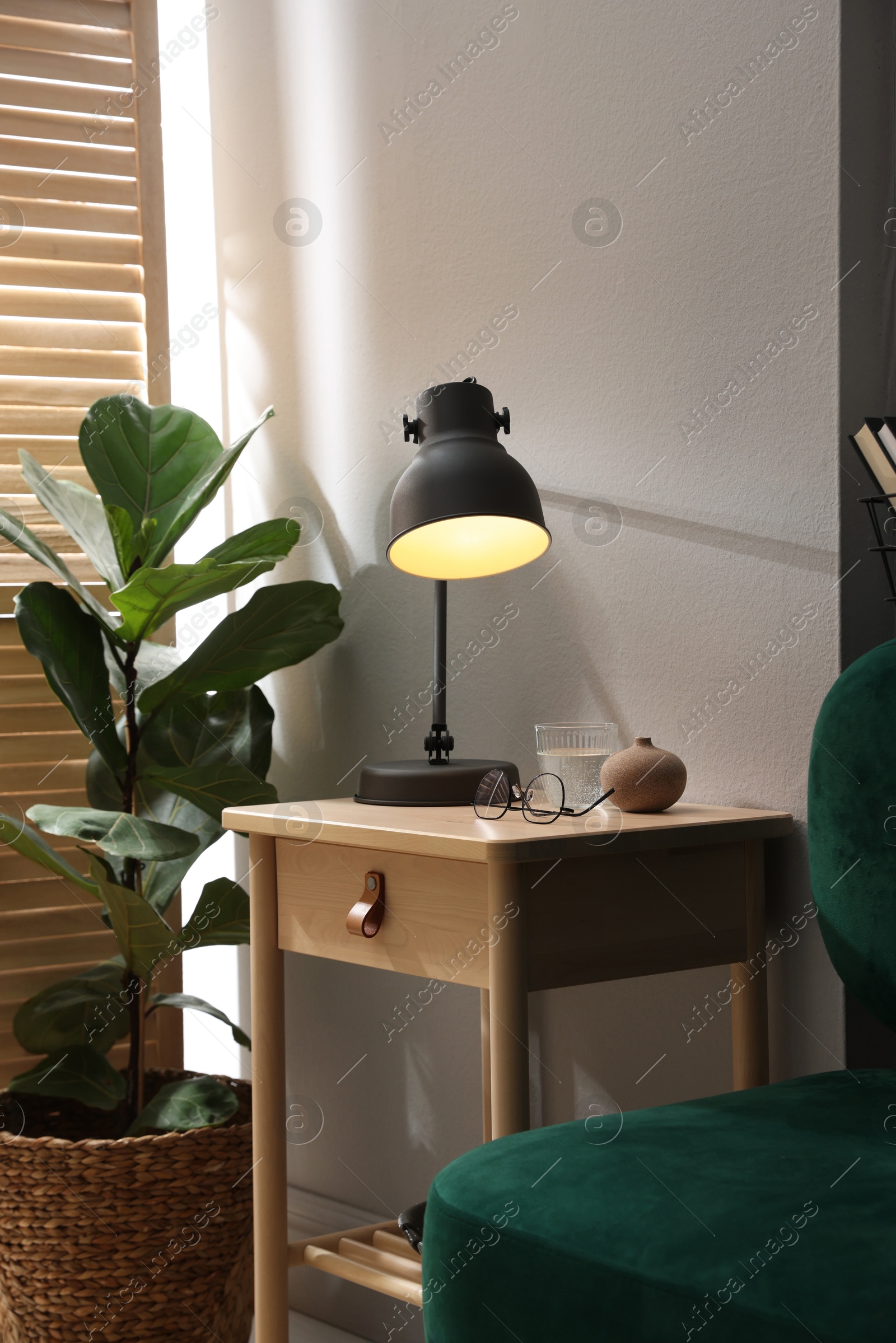 Wooden side table with glass of water, lamp and glasses indoors Photo of Wooden side table with glass of water, lamp and glasses indoors